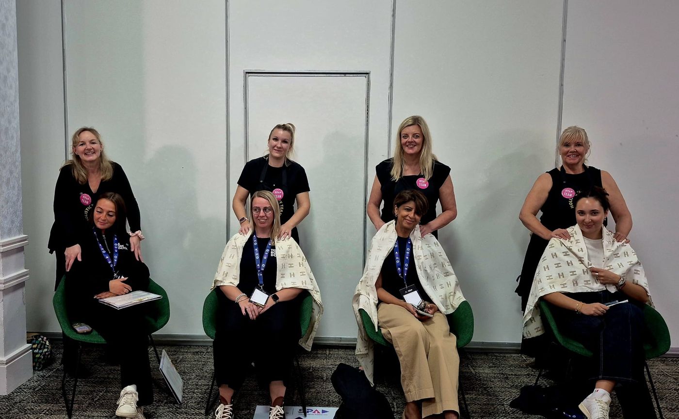 Four therapists standing behind four seated delegates, giving neck and shoulder massages